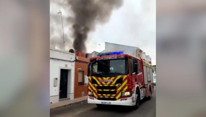 Vivienda incendiada en Montijo junto a un camión de los bomberos que trabaja en su extinción