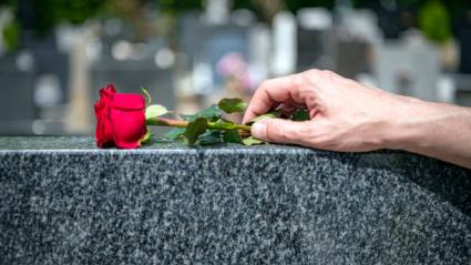 Una mano deposita una rosa en una tumba de un cementerio