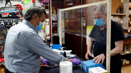 El trabajador de una ferretería atiende a un cliente con guantes, mascarilla y una pantalla protectora