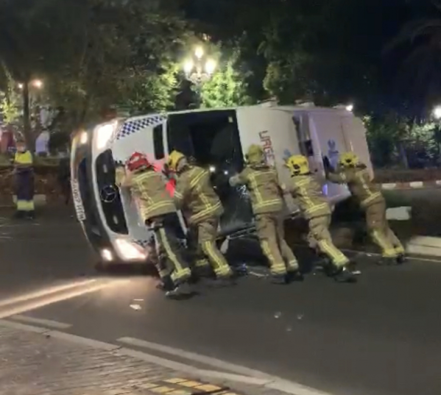 Bomberos empujando una ambulancia volcada tras un accidente