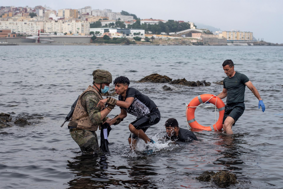 Un soldado del Ejército ayuda a dos migrantes a salir del agua en la playa de El Tarajal. La frontera entre España y Marruecos en la ciudad española de Ceuta