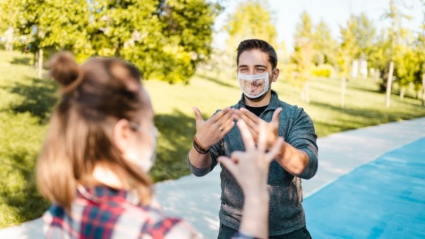 dos personas hablando en lengua de signos con mascarillas transparente que permiten lectura labial