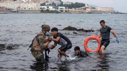 Un soldado del Ejército ayuda a dos migrantes a salir del agua en la playa de El Tarajal. La frontera entre España y Marruecos en la ciudad española de Ceuta