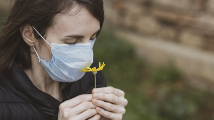 Mujer con mascarilla huele una flor