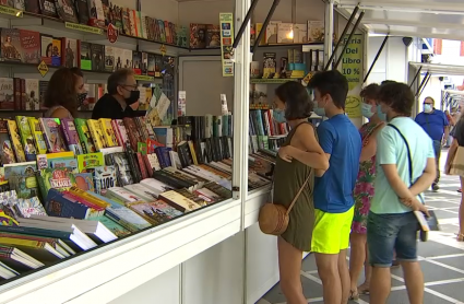 Varias personas viendo libros en una caseta de la feria del libro